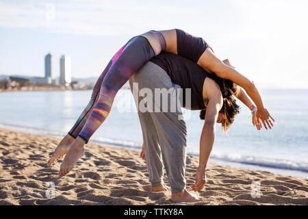 Man carrying woman on back while doing yoga on beach Stock Photo