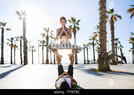 Couple performing yoga on footpath at beach during summer Stock Photo