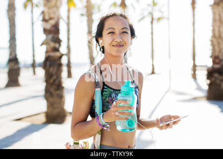 Portrait of happy sporty woman holding water bottle on footpath during summer Stock Photo