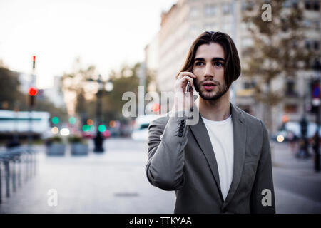 businessman talking on mobile phone while standing on footpath in city Stock Photo