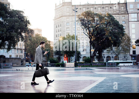 Man using mobile phone while walking on pavement Stock Photo
