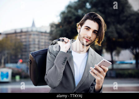 Portrait of businessman carrying bag while using mobile phone Stock Photo