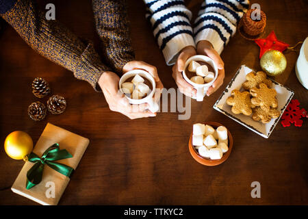 Cropped image of couple having marshmallow coffee with cookies at table Stock Photo