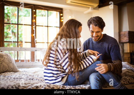 Happy couple using phone while sitting on alcove window seat at home Stock Photo