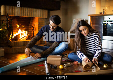 Couple wrapping gift boxes on floor by fireplace at home Stock Photo