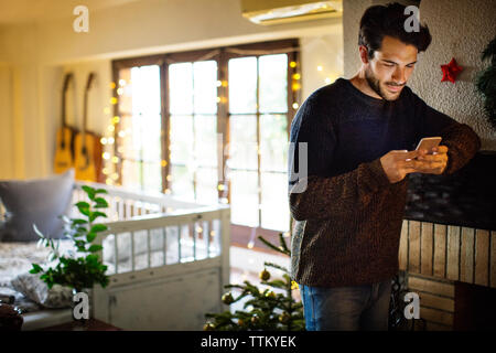 Thoughtful man using smart phone while standing at home during christmas Stock Photo