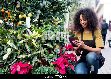 Female entrepreneur using tablet computer while crouching at market stall Stock Photo