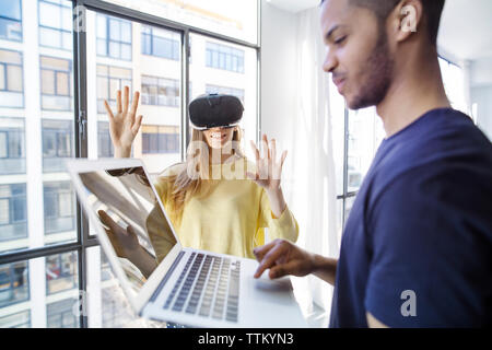 businesswoman examining virtual reality simulator while male colleague using laptop Stock Photo