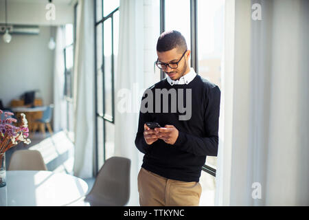 businessman using mobile phone while standing by window at office Stock Photo