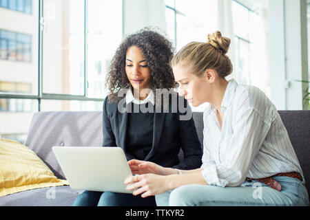 Female colleagues discussing while using laptop computer on sofa in office Stock Photo