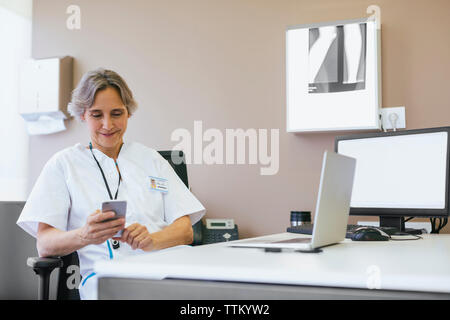 Senior female doctor using mobile phone while sitting at hospital Stock Photo