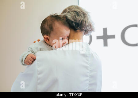 Rear view of doctor carrying baby boy against wall at hospital Stock Photo