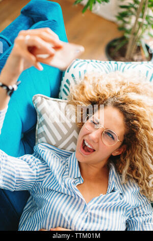High angle view of cheerful young woman taking selfie through smart phone while lying on sofa at home Stock Photo