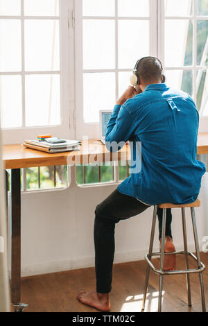 Full length rear view of man working at home office by window Stock Photo
