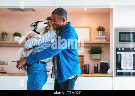 Affectionate multi-ethnic couple playing with Siberian Husky at home Stock Photo
