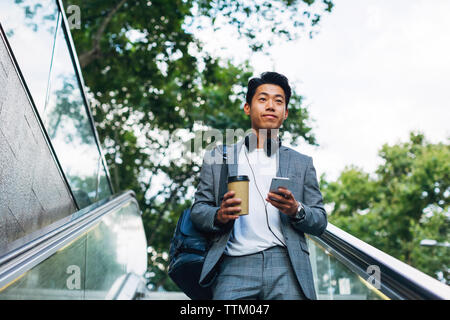 Low angle view of businessman looking away while standing on escalator Stock Photo