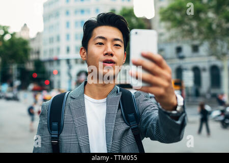 businessman with backpack taking selfie through smart phone while standing on footpath Stock Photo