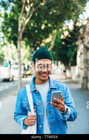 Happy man using smart phone while standing at sidewalk Stock Photo