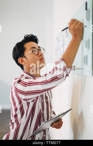 Serious businessman holding clipboard while writing on whiteboard in office Stock Photo