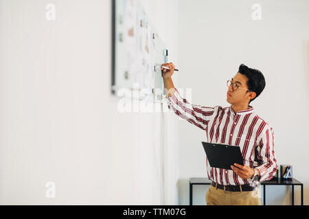 businessman holding clipboard while writing on whiteboard in office Stock Photo