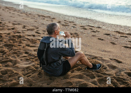 High angle view of man drinking water while sitting at beach Stock Photo