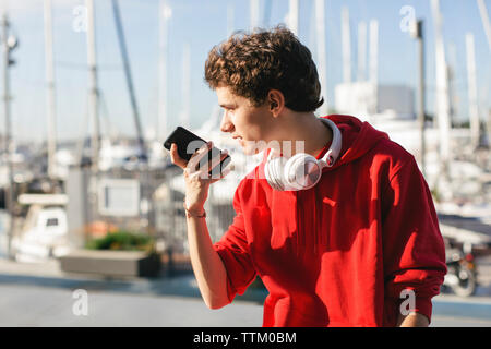 Teenage boy looking away while holding smart phone during sunny day Stock Photo