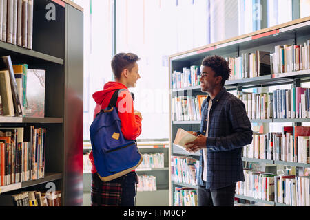 Male friends talking while standing in library Stock Photo