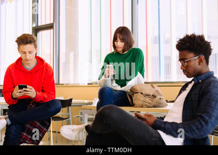 students using mobile phones while sitting in library Stock Photo