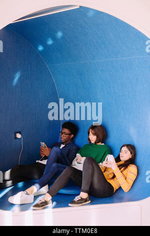 Friends using smart phones while sitting at library Stock Photo
