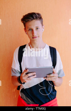 Portrait of man using tablet computer while standing against orange wall at library Stock Photo