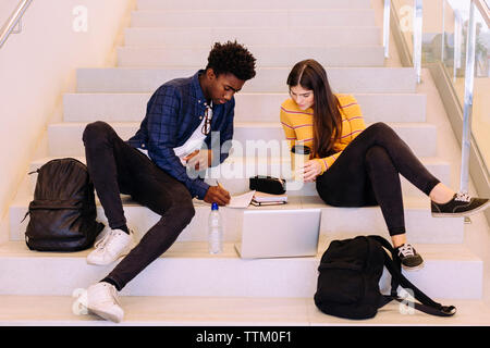 Friends discussing while sitting on steps at library Stock Photo