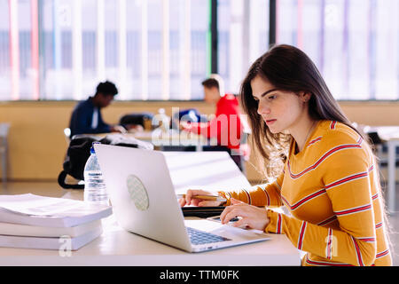 Side view of woman using laptop while male friends studying in background at library Stock Photo