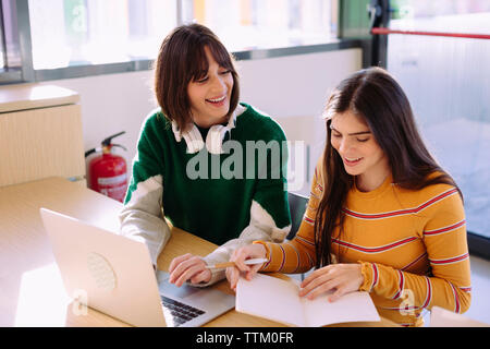 High angle view of female friends discussing over laptop computer in library