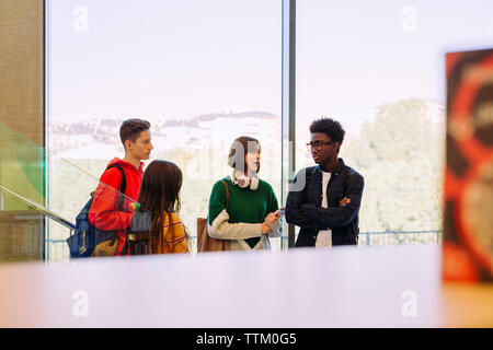 Friends talking while standing in corridor at library Stock Photo