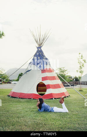 Side view of woman relaxing on grassy field against tent Stock Photo