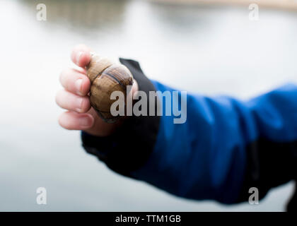 Cropped hand of child holding snail against lake Stock Photo