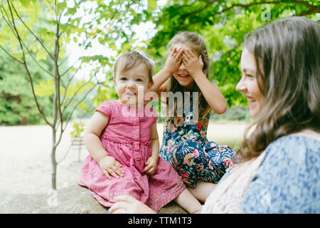 Happy mother standing by daughters sitting on log against trees in forest Stock Photo