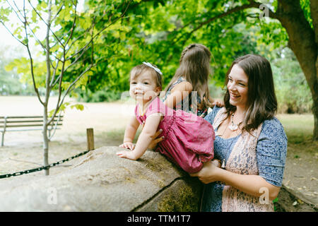 Happy mother standing by cute daughters sitting on log in forest Stock Photo