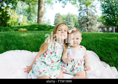 Two sisters sit together on a blanket outside Stock Photo