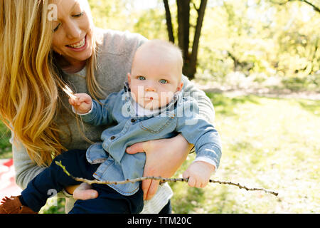 A mom holds her baby son while he holds a stick Stock Photo