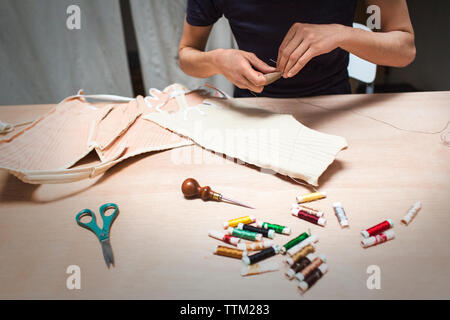 Cropped image of fashion designer stitching fabric at table in workshop Stock Photo