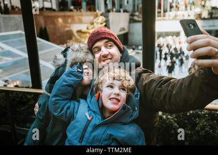 Happy father with sons making face while taking selfie against window in city Stock Photo