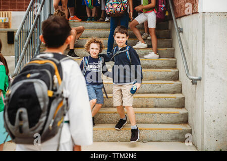 Brothers with backpacks standing on steps in school Stock Photo