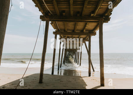 Diminishing perspective of pier over sea against sky during sunny day Stock Photo