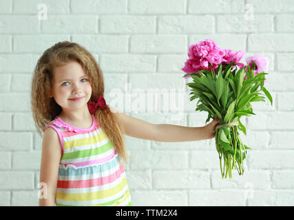 Beautiful girl holding fresh peonies bouquet on brick wall background Stock Photo