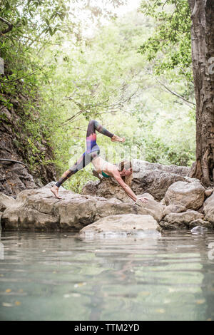 Woman practicing yoga on rocks at lakeshore Stock Photo