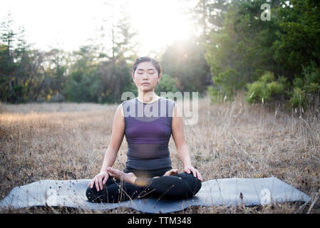 Woman meditating while sitting on exercise mat at field Stock Photo