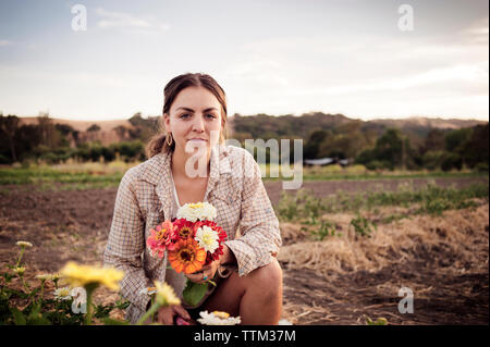 Portrait of confident female farmer holding beautiful flowers on field Stock Photo