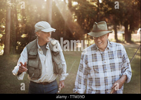 Happy senior men holding fishing rods while walking in forest Stock Photo