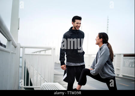 Happy athletes talking while exercising on Bay Bridge against sky Stock Photo
